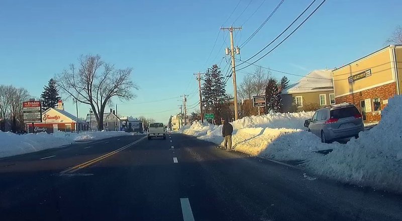 A pedestrian walks in the right lane of MassDOT's Route 18/Main Street in Weymouth because the sidewalks are buried in deep snowbanks.