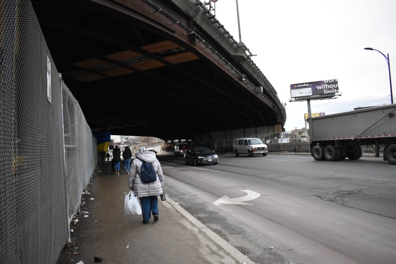 Pedestrians walk along the narrow sidewalk on Maffa Way, an off-ramp from I-93 and the primary walking route between Sullivan Square Orange Line stop and East Somerville.