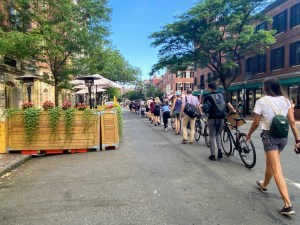 A chain of people, mostly with bikes, line up along the right lane of Charles Street in Beacon Hill to form a temporary "people-protected" bike lane.
