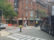 a flagger wearing a bright reflective vest stands in the intersection and waves a charter bus through