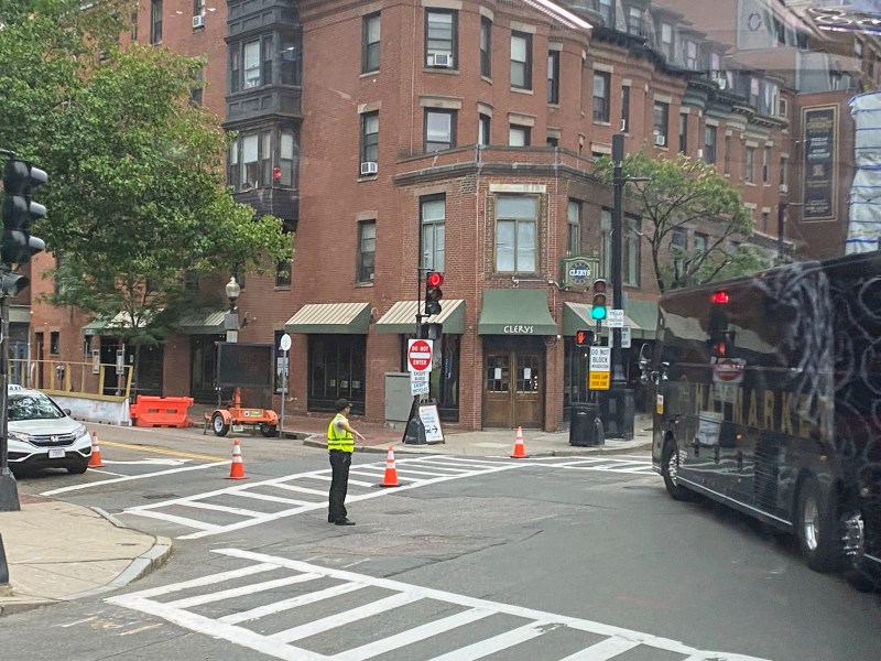 a flagger wearing a bright reflective vest stands in the intersection and waves a charter bus through