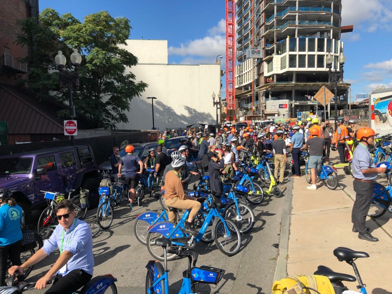 A crowd of people and Bluebikes gathers near Boylston Street